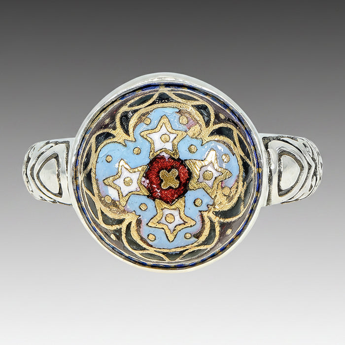 A Victorian Antique Inlay Button Ring with a floral design, featuring a central red stone surrounded by blue and gold patterns, set in a silver band.