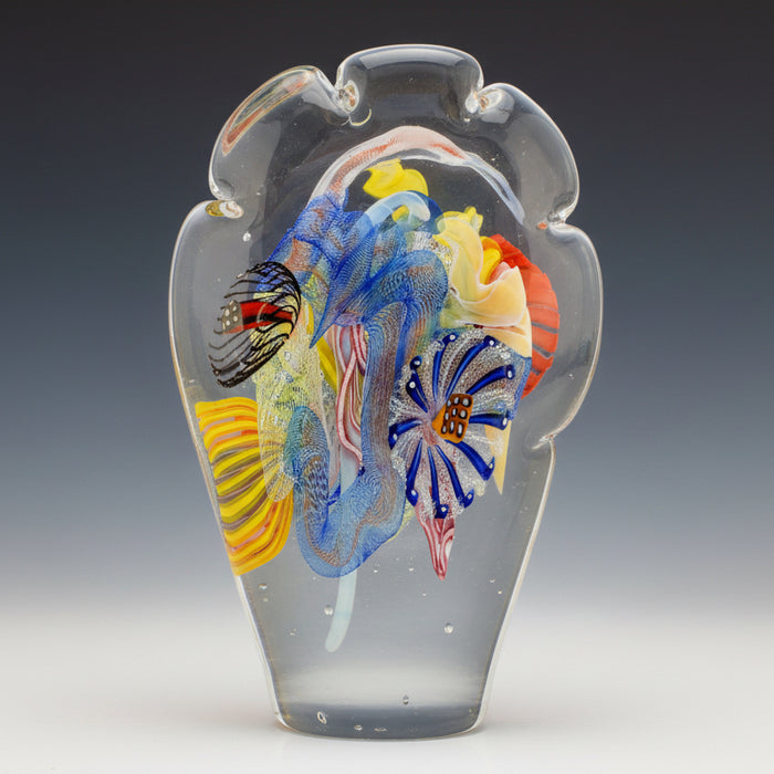 A multicolored flattened paperweight with a cloud shape made by Hunting Studio Glassworks.