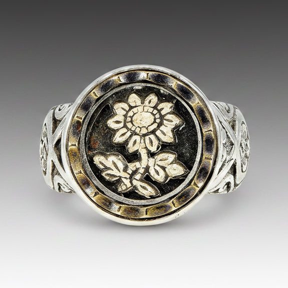 A sterling silver ring with a central Victorian daisy carved button, surrounded by a decorative patterned band.