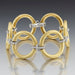 Gold bracelet with interlocking rings and diamond accents on a gray background