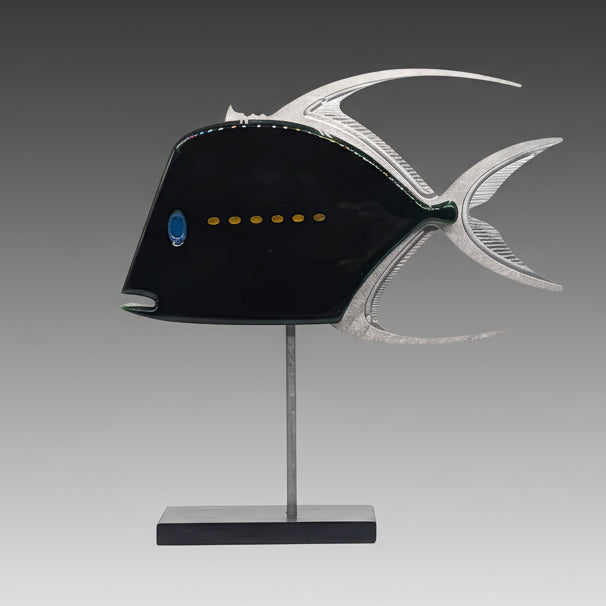A mixed media sculpture of a fish with a predominantly black body, featuring a yellow dot stripe, silver fins, and a blue eye detail, displayed on a metal stand.