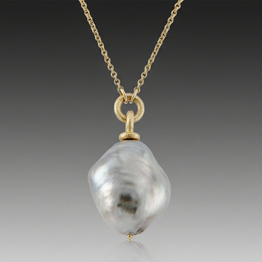 A Tahitian Baroque pearl necklace strung along an 18k yellow gold chain with a gold cap and a loop for attachment, displayed against a marble background.