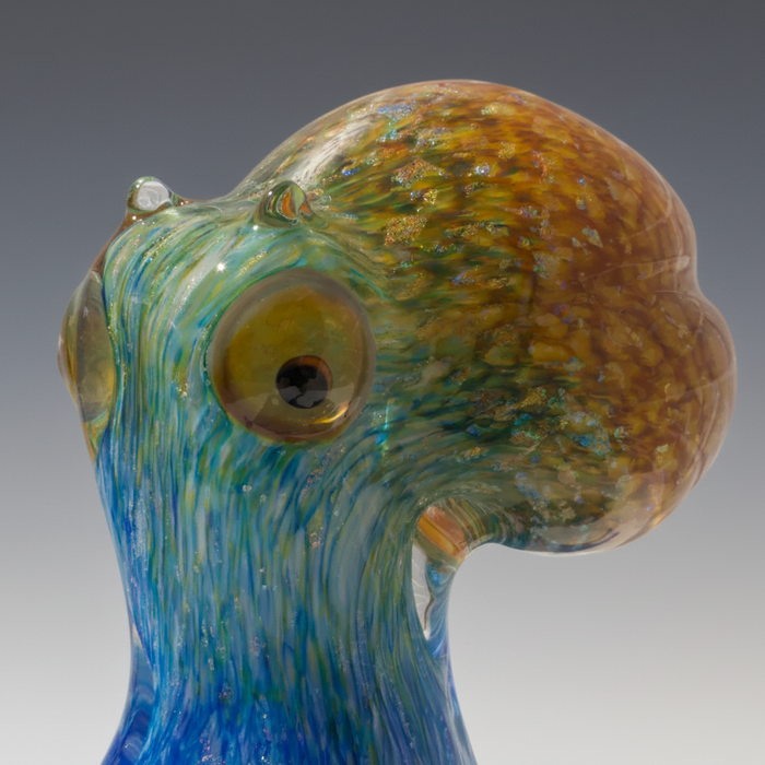 Glass sculpture of a bird with blue and brown colors against a white background