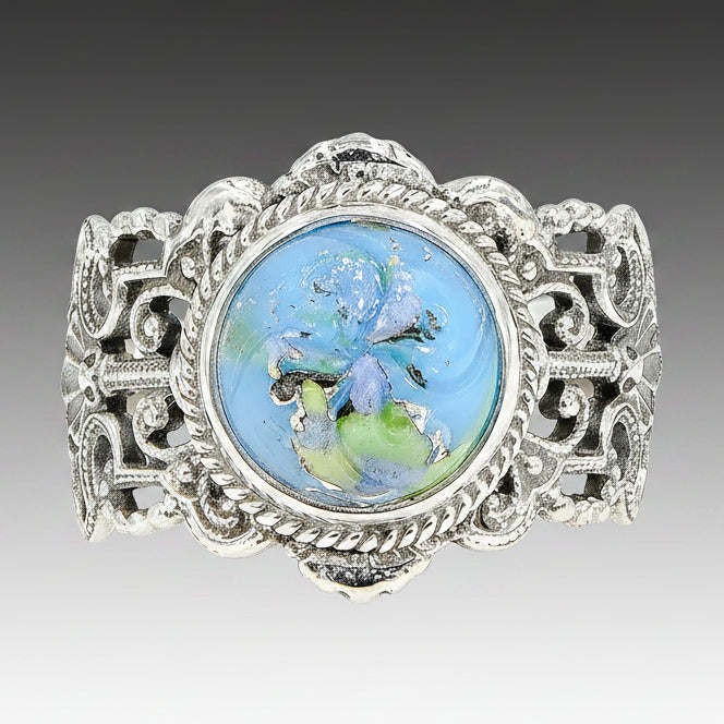 A sky blue Leo Popper glass button ring set in sterling silver with intricate filigree work, displayed against a white background.