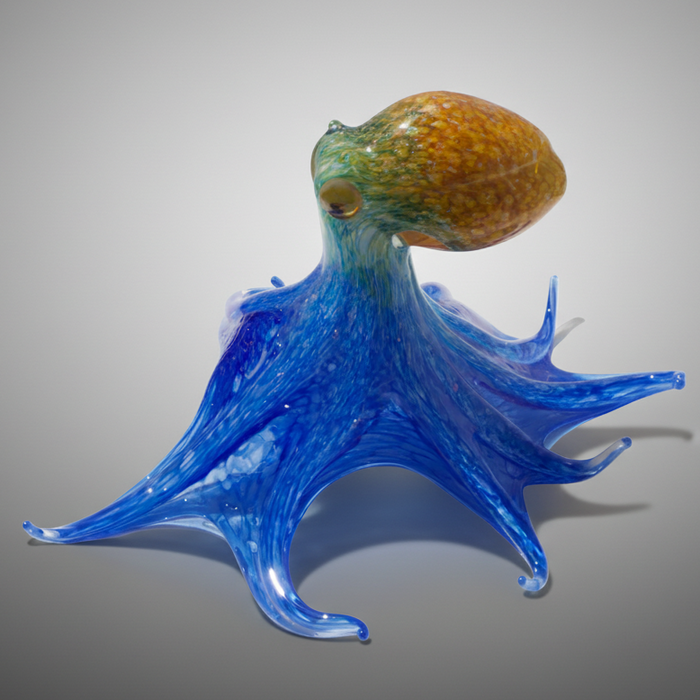 Glass sculpture of an octopus with a textured head on a white surface with a brick wall background