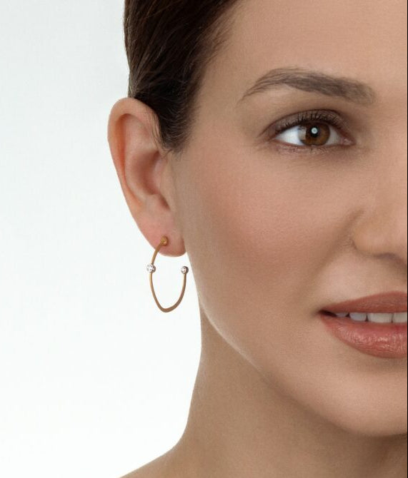Close-up of a woman wearing gold hoop earrings with a plain background