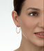 Close-up of a woman wearing gold hoop earrings with a plain background