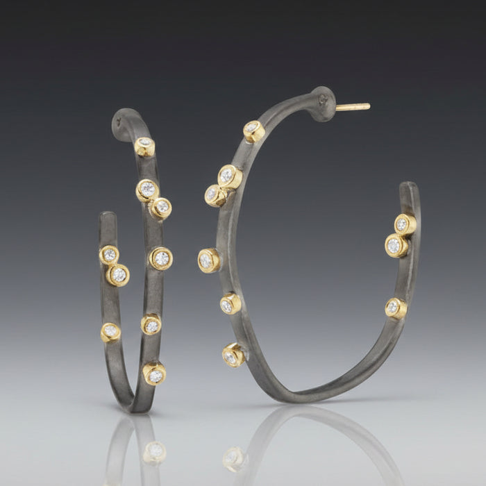 A pair of medium-sized hoop earrings with oxidized sterling silver, 18K yellow gold accents, and embedded diamonds.