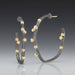 A pair of medium-sized hoop earrings with oxidized sterling silver, 18K yellow gold accents, and embedded diamonds.