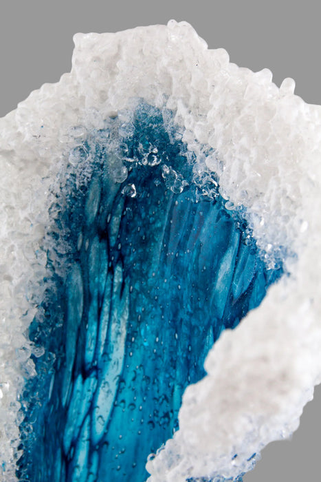Close-up of a crystal with blue interior and white exterior on a gray background