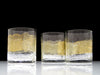 Three handblown glasses with a ripple texture and gold and white coloring, displayed on a clear surface.