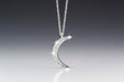 A crescent moon-shaped necklace with a central round brilliant cut diamond in a pave setting, suspended from an adjustable chain.