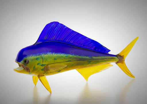 A handblown glass art piece in the shape of a fish with vibrant shades of blue and green with yellow detail.