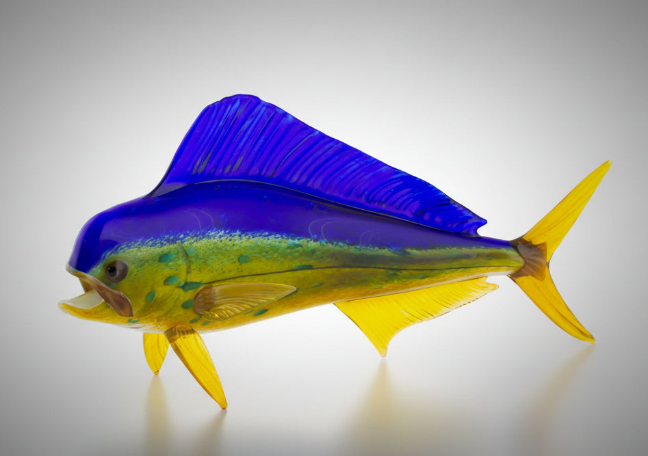 A handblown glass art piece in the shape of a fish with vibrant shades of blue and green with yellow detail.