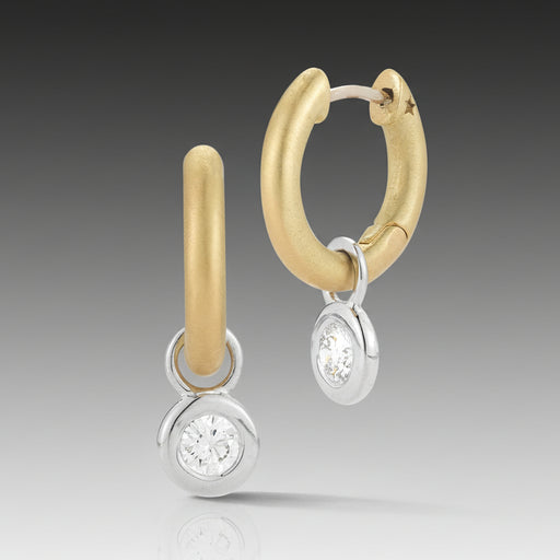 A pair of Mercer Diamond Single Drop Huggie Earrings featuring a 18k brushed yellow gold hoop with a removable 18k high polish white gold charm bezel and a round, brilliant cut diamond.