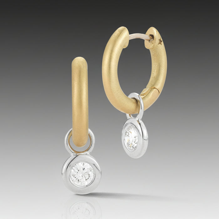 A pair of Mercer Diamond Single Drop Huggie Earrings featuring a 18k brushed yellow gold hoop with a removable 18k high polish white gold charm bezel and a round, brilliant cut diamond.