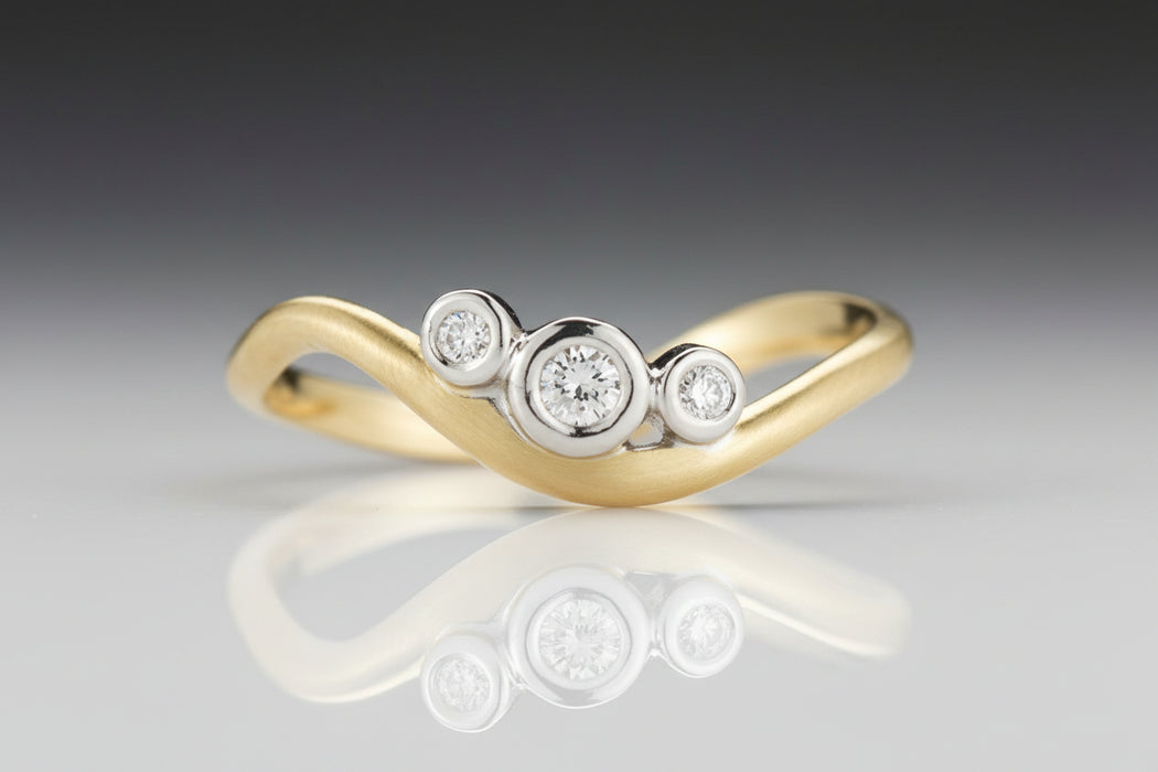 A three-stone diamond ring with a gold band, featuring two white gold settings with diamonds in a v-shaped design.